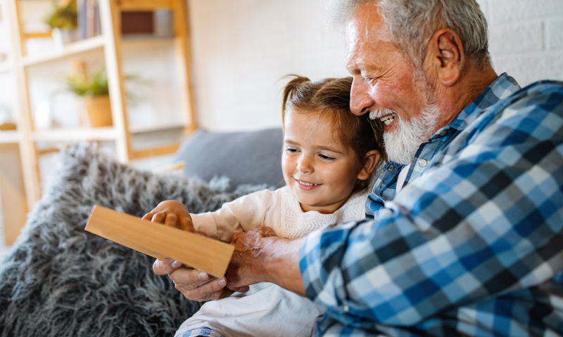 A man sitting on the couch with his grand daughter with a book