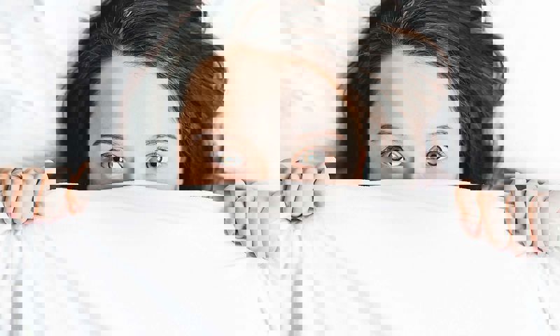 Womans eye peaking out from under the bed covers