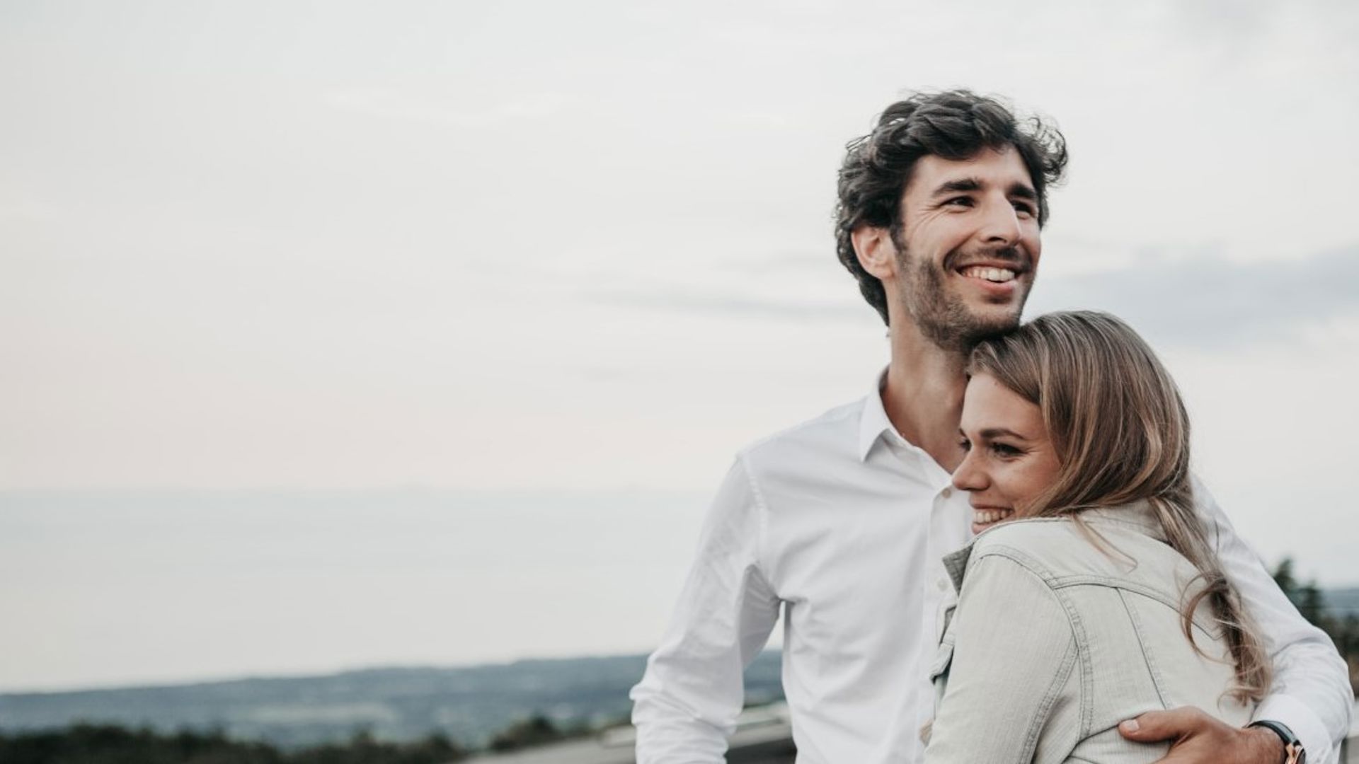 Man and woman couple on the beach cuddling and looking happy