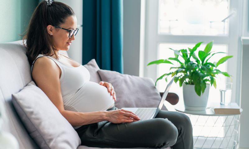 Pregnant woman wearing glasses using laptop