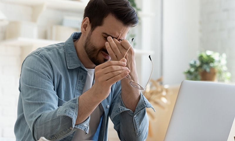 Man who wears glasses rubbing his eyes after experiencing dry eyes