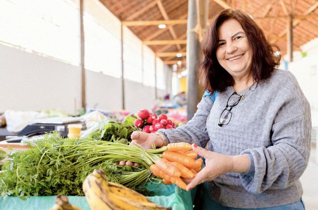 Mature woman smiling and selecting carrots at a market.