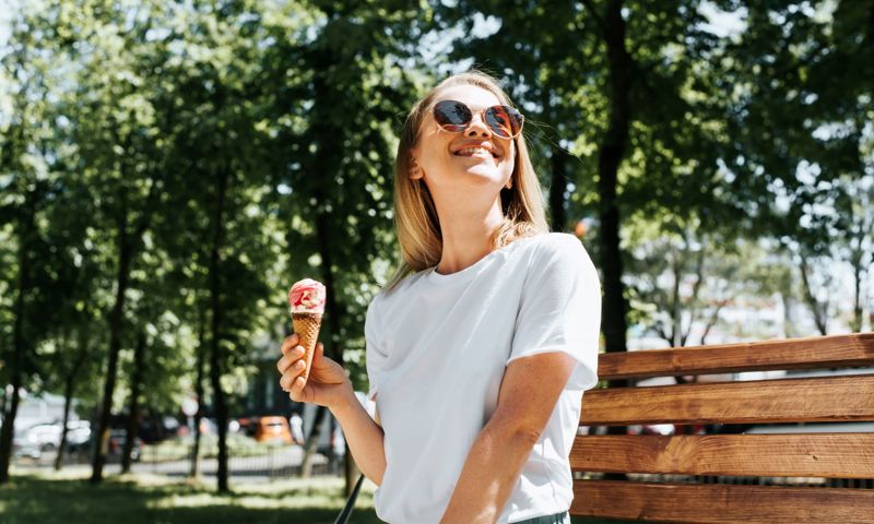 A smiling woman wearing sunglasses and holding an ice cream.