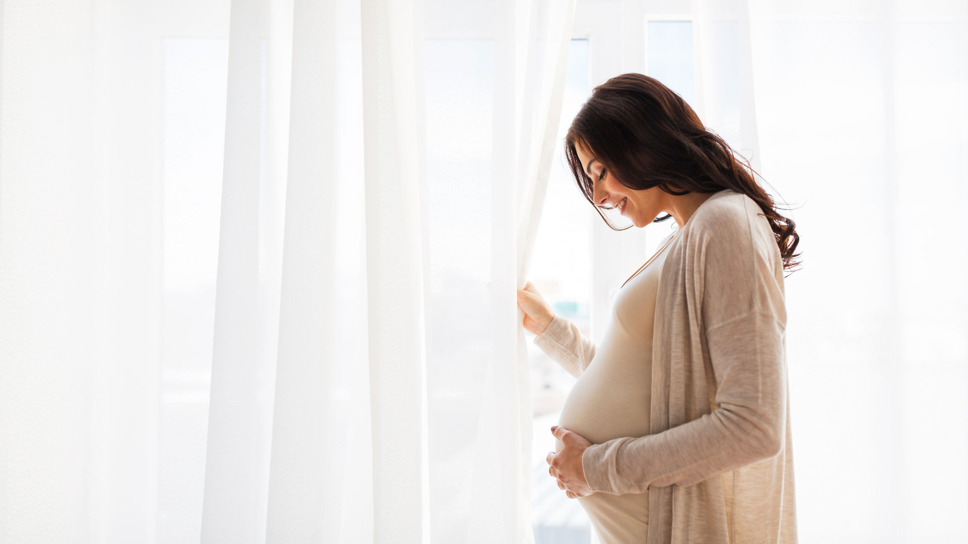 Pregnanct lading holding her belly in front of window