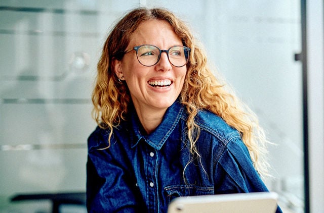 Young lady wearing denim and stylish glasses smiling across a table.