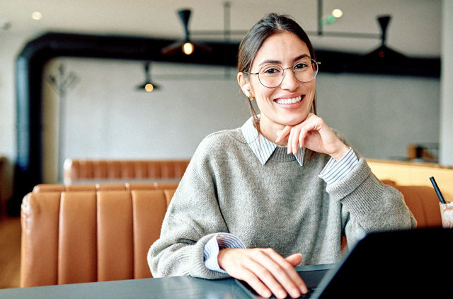 Young woman smiling while at a cafe with her laptop.