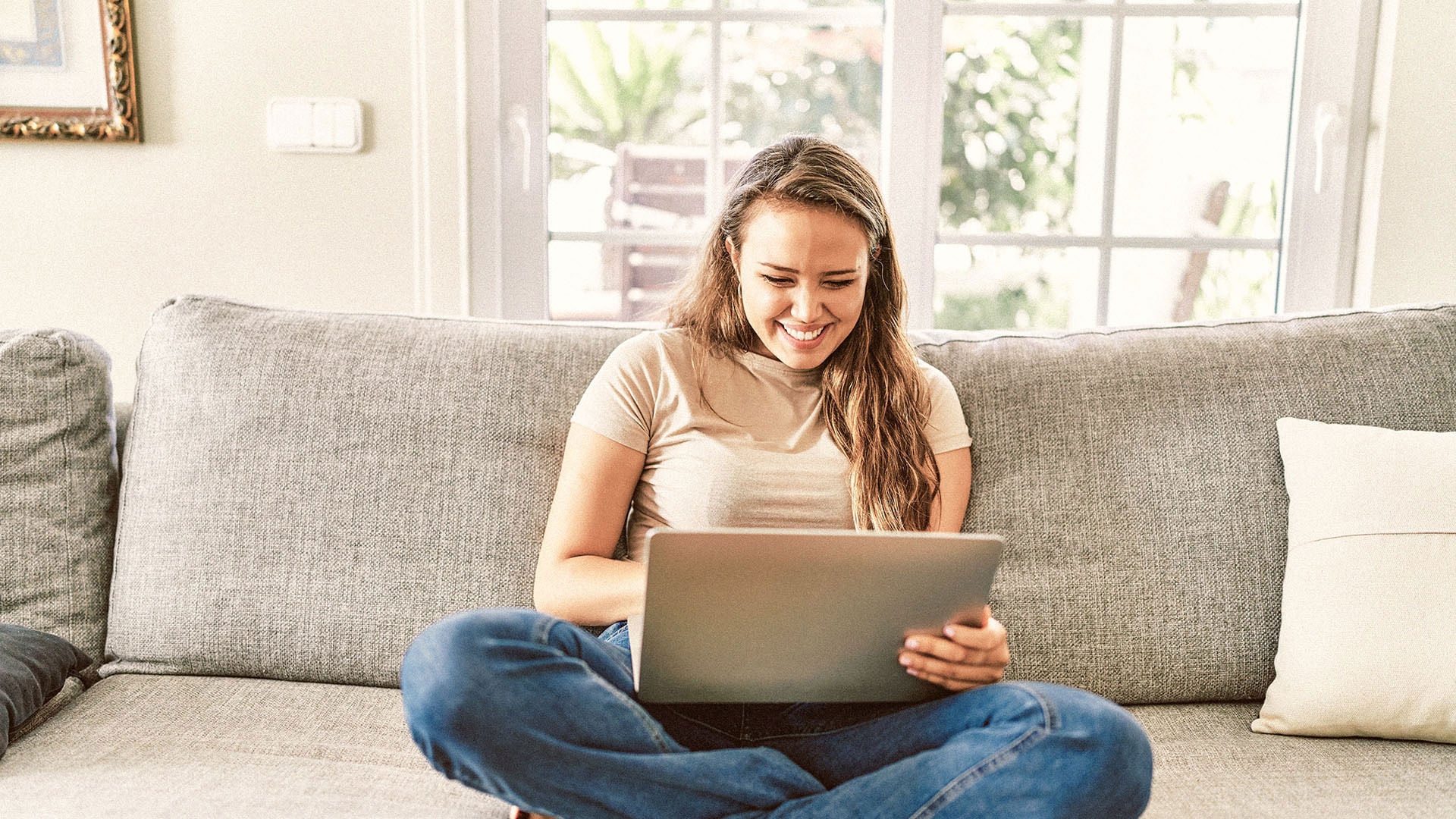 Girl in late 20s sitting on the couch using a laptop