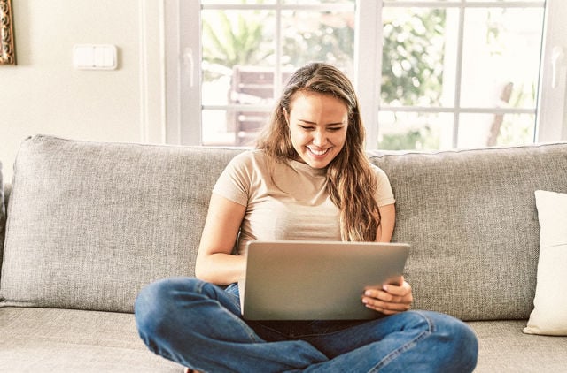 Girl in late 20s sitting on the couch using a laptop