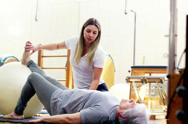 Woman helping elderly person with rehab using an exercise ball