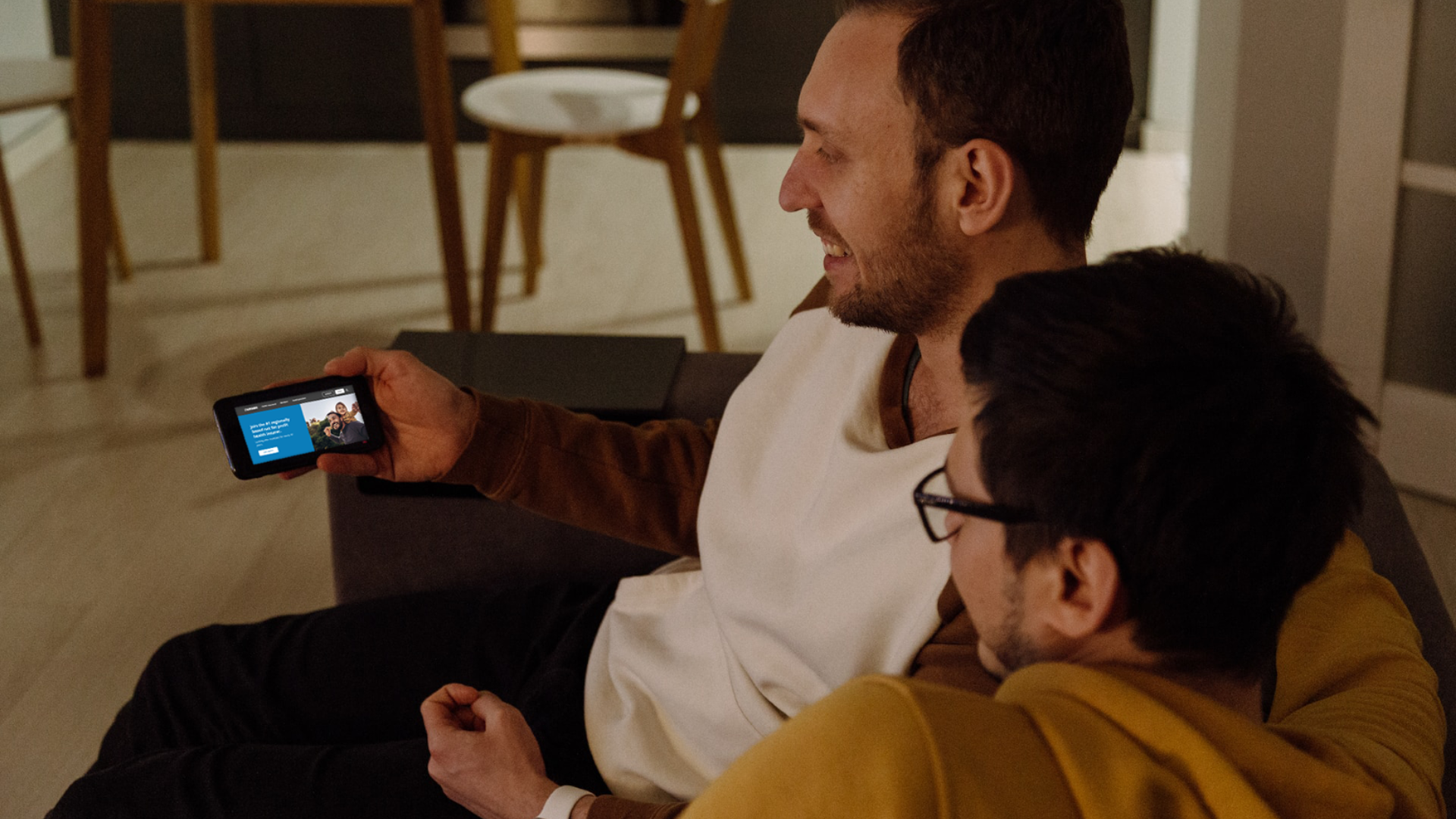 Two men sitting and looking at the GMHBA website on their mobile phone
